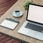 A minimalist outdoor workstation with laptop, coffee, and tablet on a rustic table.